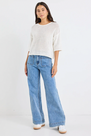 Woman wearing a white textured top and light blue jeans on a white background