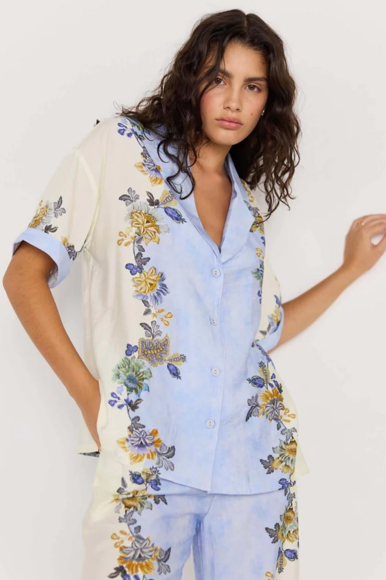 Lucia Resort Shirt - Blue &amp; Cream Floral, by Minkpink

The Lucia Resort Shirt is an easy, breezy staple for warm-weather days. Featuring a relaxed fit, short sleeves, and a button-down front, it’s adorned with a watercolour blue and cream base scattered with vibrant floral prints. The notched collar adds a laid-back touch, perfect for pairing with the matching Lucia pants or styling separately.