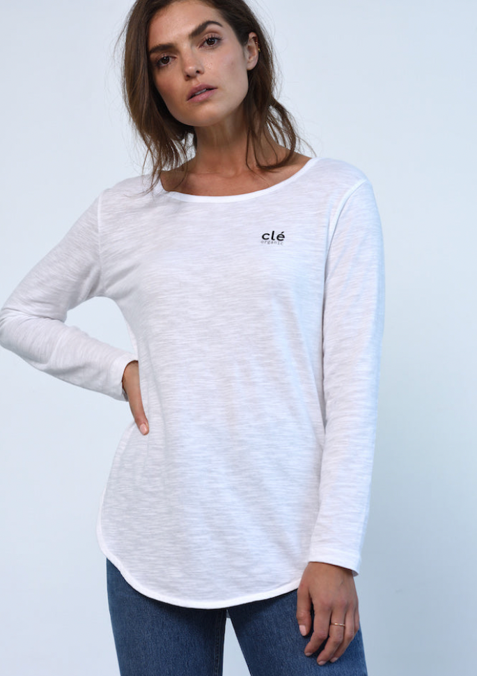 Layla L/S Tee - White, by Clé  The Layla L/S Tee features a simple scoop neckline and longer length front and back hem, with flattering scooped sides and tasteful small black logo on front chest.  This style is semi tapered through the body making it a great layering piece worn under a sweater, or the perfect long sleeve basic on its own.  We love her worn under our Ulverstone Sweats and paired with the Golden Stripes Jogger, for the ultimate off-duty look.