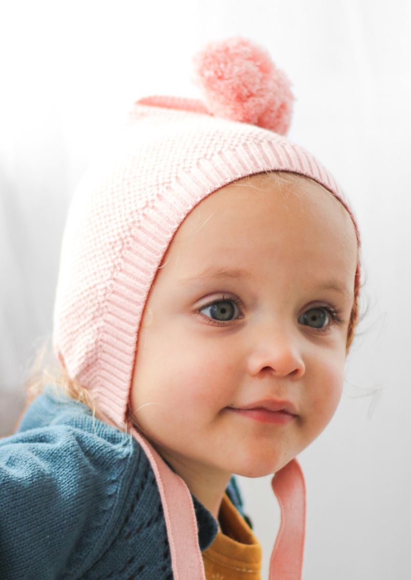 Knit Bonnet - Pink - Burrow and Be This sweet wee knit bonnet is a welcome new addition to our Collection - we think you will love it just as much as we do!  Made from 100% organic cotton knit, it features an adorable pom pom and an under the chin tie to keep it nice and snug.